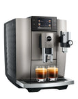 A Jura commercial-style espresso machine in brushed stainless steel with a black textured side panel, shown with two espresso cups on the drip tray against a plain white background.