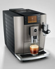 A Jura commercial-style espresso machine in brushed silver and black, shown with a glass of espresso on the drip tray against a light gray studio background.