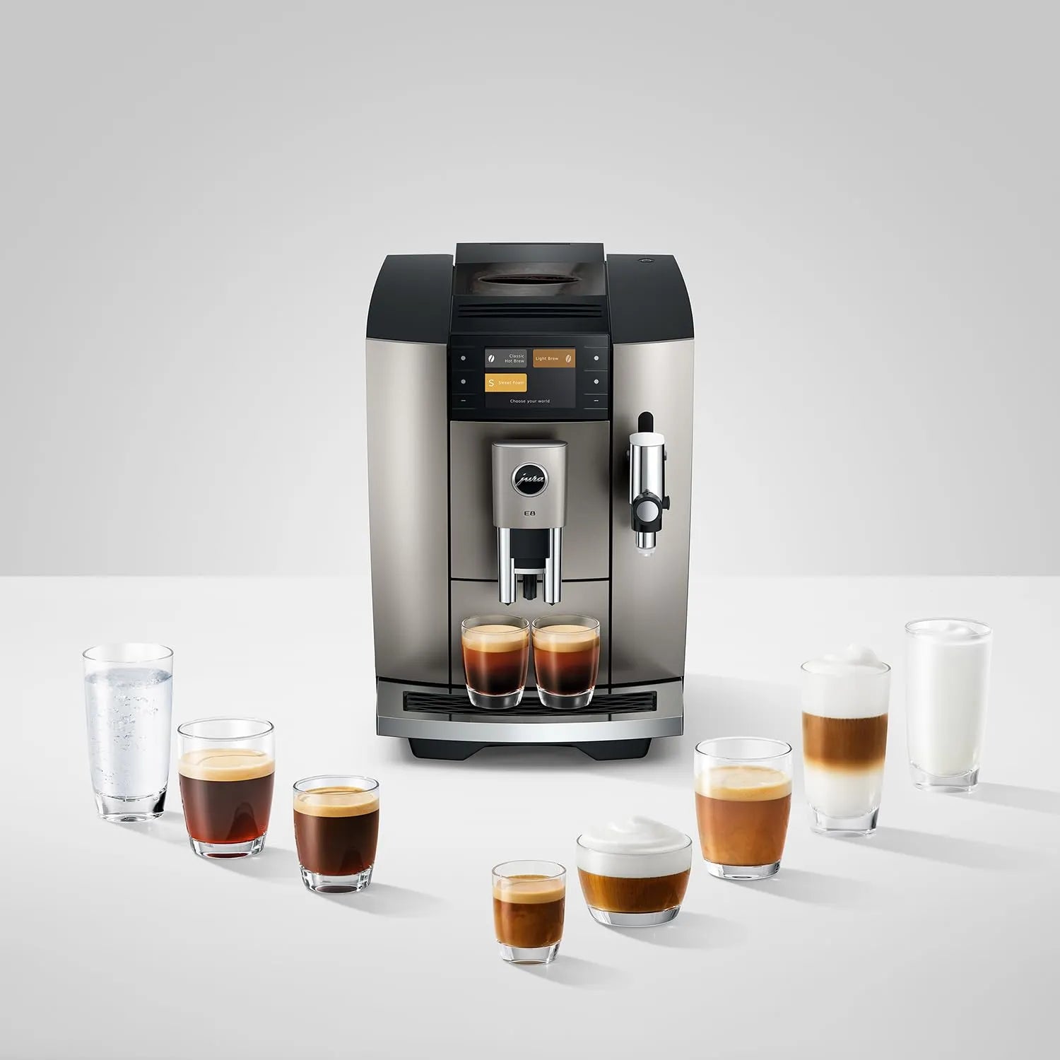 A stainless steel and black espresso machine centered on a light gray studio background, with several glass cups of coffee and milk drinks arranged around it on a white surface.