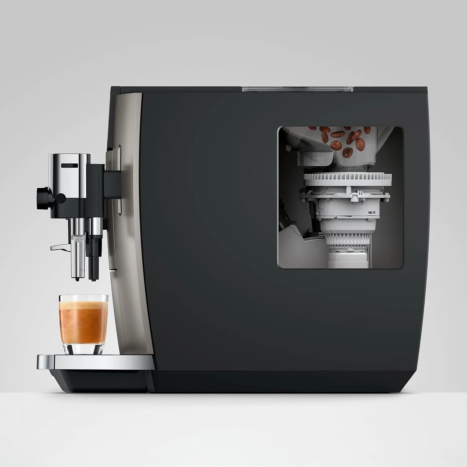 A modern espresso machine in matte black and stainless steel, shown with a glass of espresso on the drip tray and a transparent window revealing the internal bean hopper.