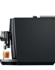 A sleek black coffee machine with a small glass cup of espresso on its tray, shown against a solid white background.