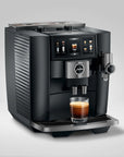 A black and stainless steel Jura coffee machine with a glass of espresso and latte underneath, set against a clean light gray background.