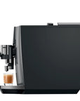 A sleek black coffee machine with a glass of espresso and milk on its drip tray, shown against a solid white background.