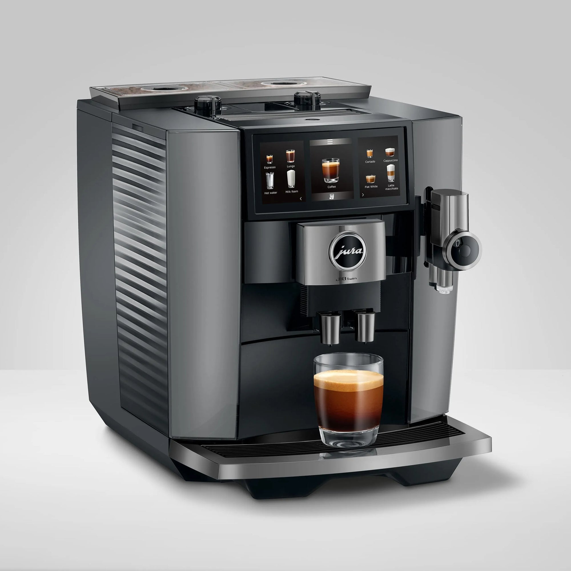A Jura coffee machine in dark gray and stainless steel, shown with a glass of espresso on its drip tray against a light gray studio background.