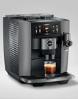 A Jura coffee machine in dark gray and stainless steel, shown with a glass of espresso on its drip tray against a light gray studio background.