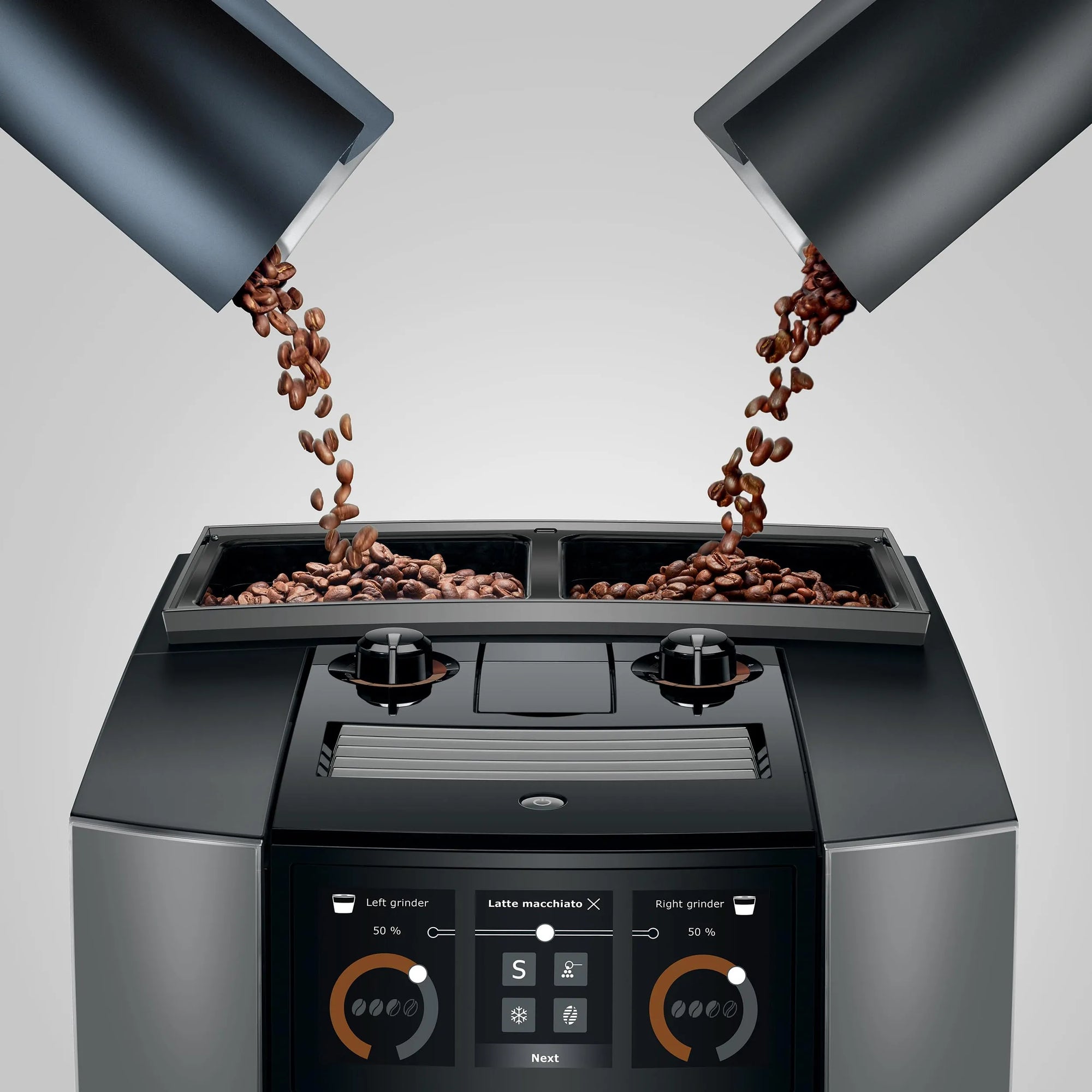 A modern espresso machine with two bean hoppers pouring coffee beans into the hopper compartments, shown against a light gray studio background.