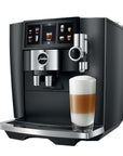 Black and silver Jura coffee machine with a glass of layered coffee on a white background