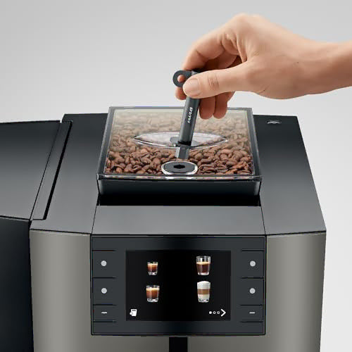 A close-up of a hand inserting a black key into a transparent bean hopper filled with roasted coffee beans on a modern espresso machine.
