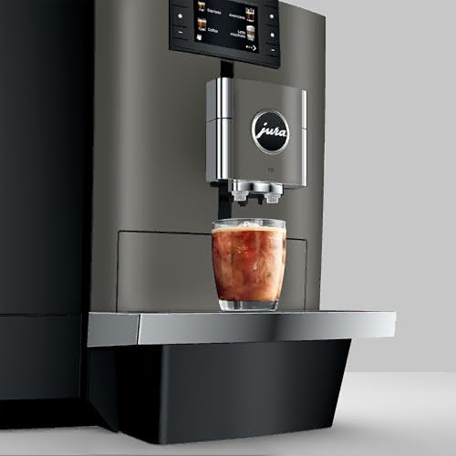 A sleek Jura commercial-style coffee machine in dark gray and black, shown dispensing an iced coffee into a clear glass on a metal tray against a light gray background.