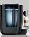 Side view of modern coffee machine with a glass of layered coffee and water filter container on a light gray background