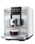 A Jura Z10 professional espresso machine in stainless steel, shown with a glass of espresso and milk on the drip tray against a white background.