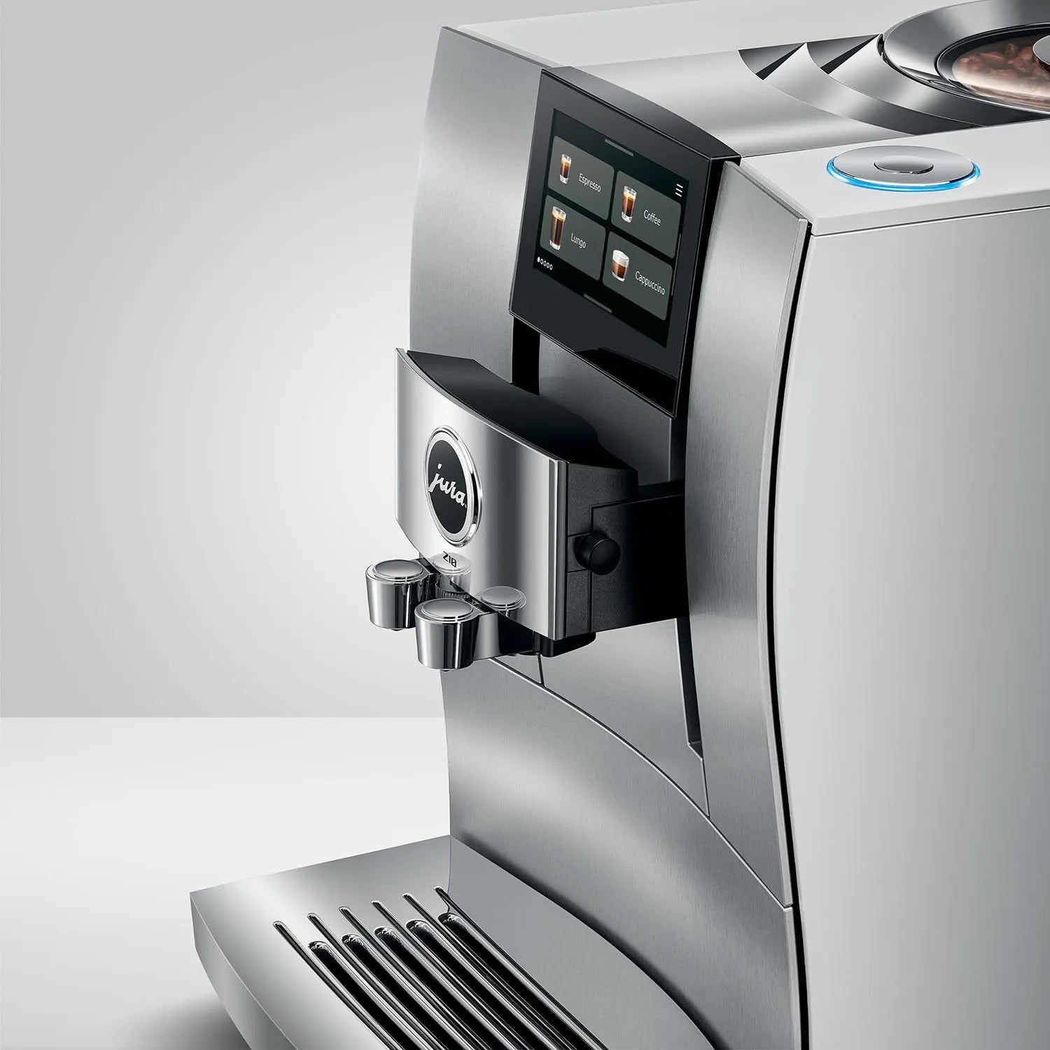 A close-up studio shot of a stainless steel Jura coffee machine, showing the front display screen, water dispenser spout, drip tray, and part of the bean hopper against a clean light gray background.