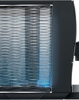 Side view of a sleek black coffee machine with a large ribbed transparent water tank and a small glass of espresso on the drip tray, shown against a plain white background.