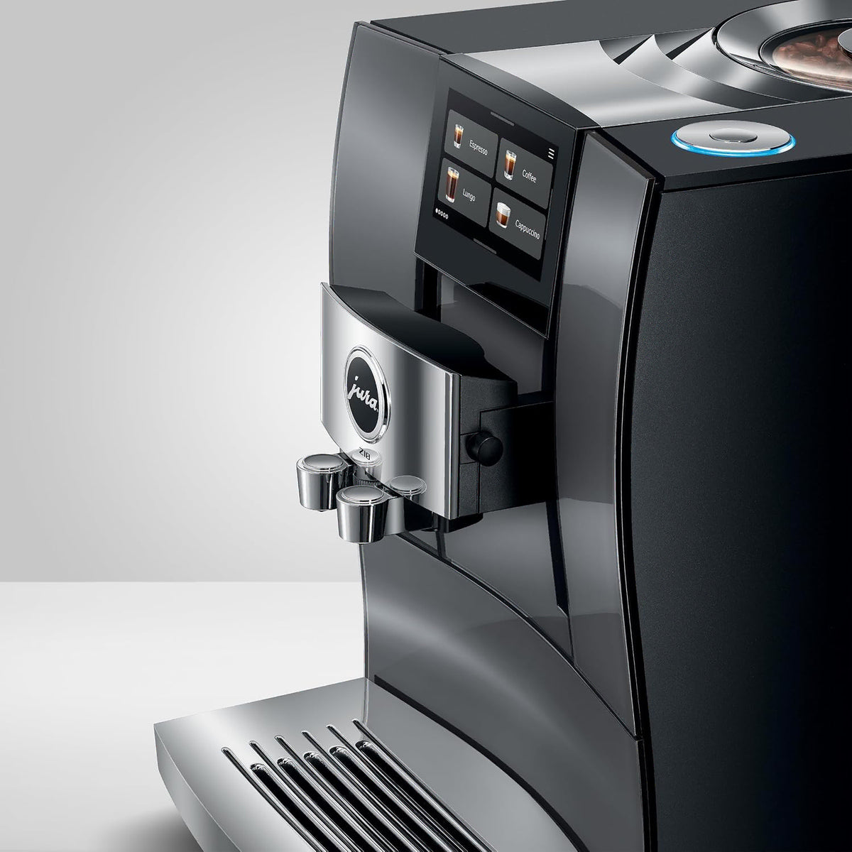 A close-up studio shot of a sleek Jura coffee machine in glossy black and silver, showing the digital touch control panel, water dispensing spouts, and drip tray against a clean white background.