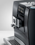 A close-up studio shot of a sleek Jura coffee machine in glossy black and silver, showing the digital touch control panel, water dispensing spouts, and drip tray against a clean white background.