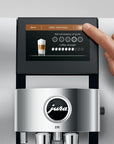 Close up of Aluminum White Jura espresso machine with a finger pressing buttons on a touchscreen coffee selection