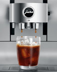 Close up of Aluminum White Jura espresso machine dripping coffee into a glass cup with ice on stand