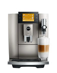 A metallic silver and black Jura coffee machine with a digital touch screen, shown next to a glass of layered latte macchiato on a white background.