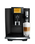 A black and silver Jura coffee machine with a digital touch screen, shown with a glass of layered latte macchiato on a white background.