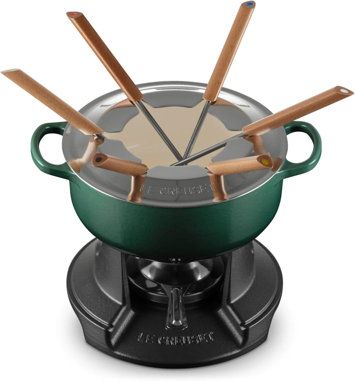 A Le Creuset fondue set featuring a dark green enameled pot with a stainless steel lid, six wooden-handled fondue forks, and a black cast-iron burner base, all shown on a white background.