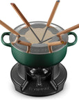 A Le Creuset fondue set featuring a dark green enameled pot with a stainless steel lid, six wooden-handled fondue forks, and a black cast-iron burner base, all shown on a white background.