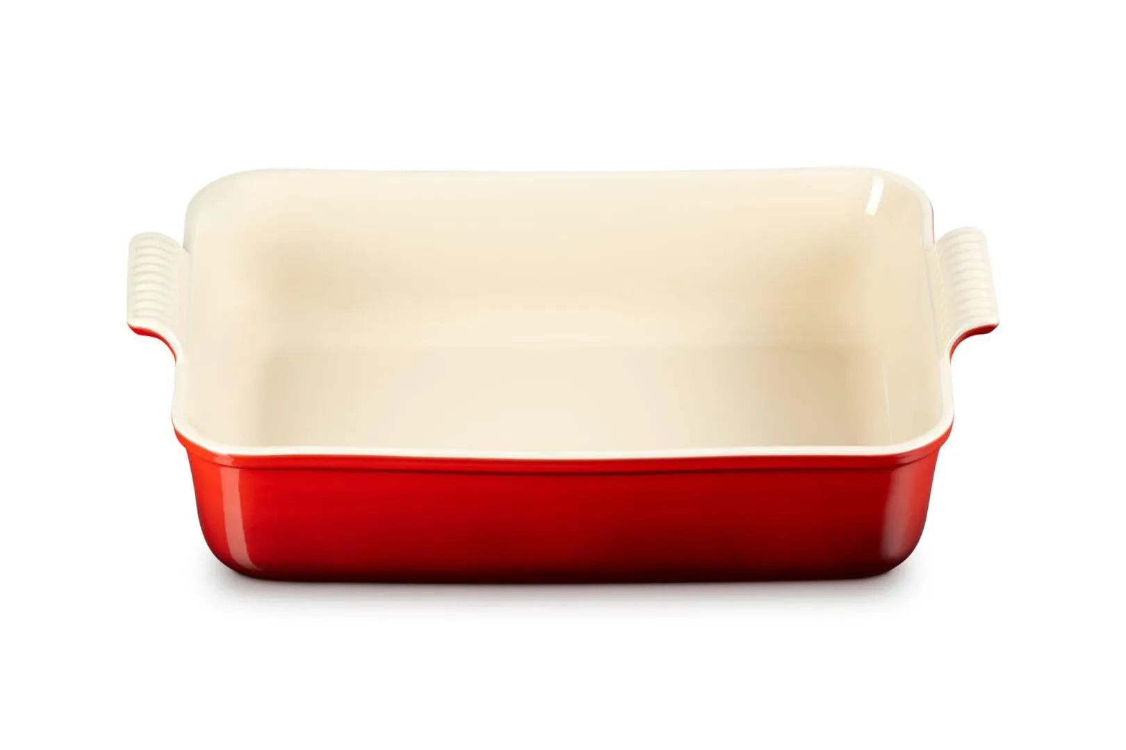 A rectangular ceramic baking dish with a glossy red exterior and a cream-colored interior, featuring integrated side handles, shown on a plain white background.