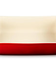 A rectangular ceramic baking dish with a glossy red exterior and a cream-colored interior, featuring integrated side handles, shown on a plain white background.