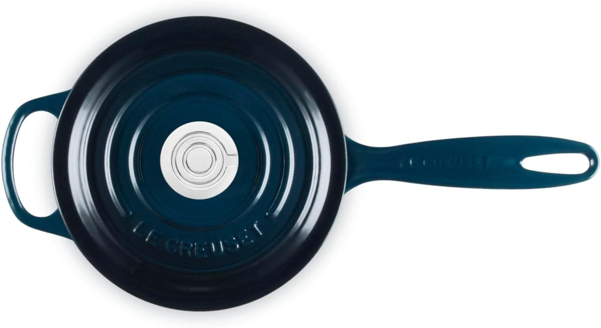 A top-down view of a Le Creuset cast iron skillet in a deep teal blue color, showing the handle, side loop, and the brand name embossed on the bottom of the lid.
