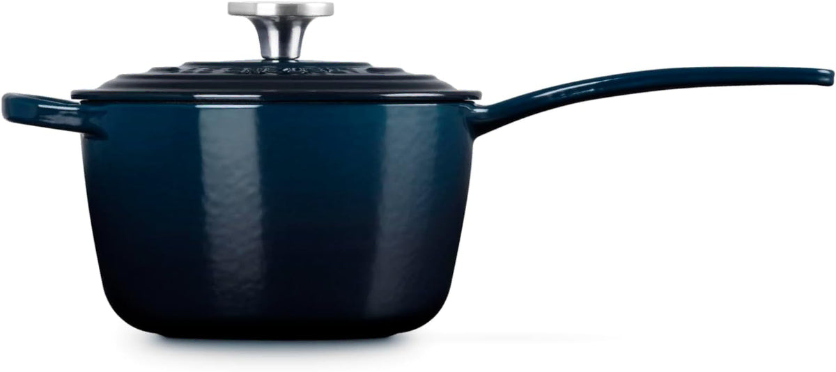Side view of a dark navy blue enameled cast iron saucepan with a matching lid and long handle, shown on a clean white background.