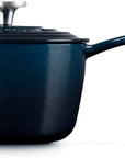 Side view of a dark navy blue enameled cast iron saucepan with a matching lid and long handle, shown on a clean white background.