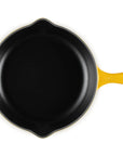 A top-down view of a cast iron skillet with a black interior and bright yellow exterior handles, isolated on a white background.