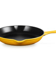 A yellow enameled cast iron skillet with a black interior, featuring a small loop handle on the left and a long straight handle on the right, shown on a solid white background.