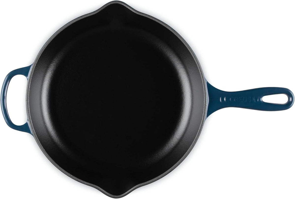 A top-down view of a cast iron skillet with a dark blue enameled handle and side handles, set against a plain white background.