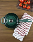 Green Le Creuset saucepan on a wooden surface with a striped towel and tomatoes in the background
