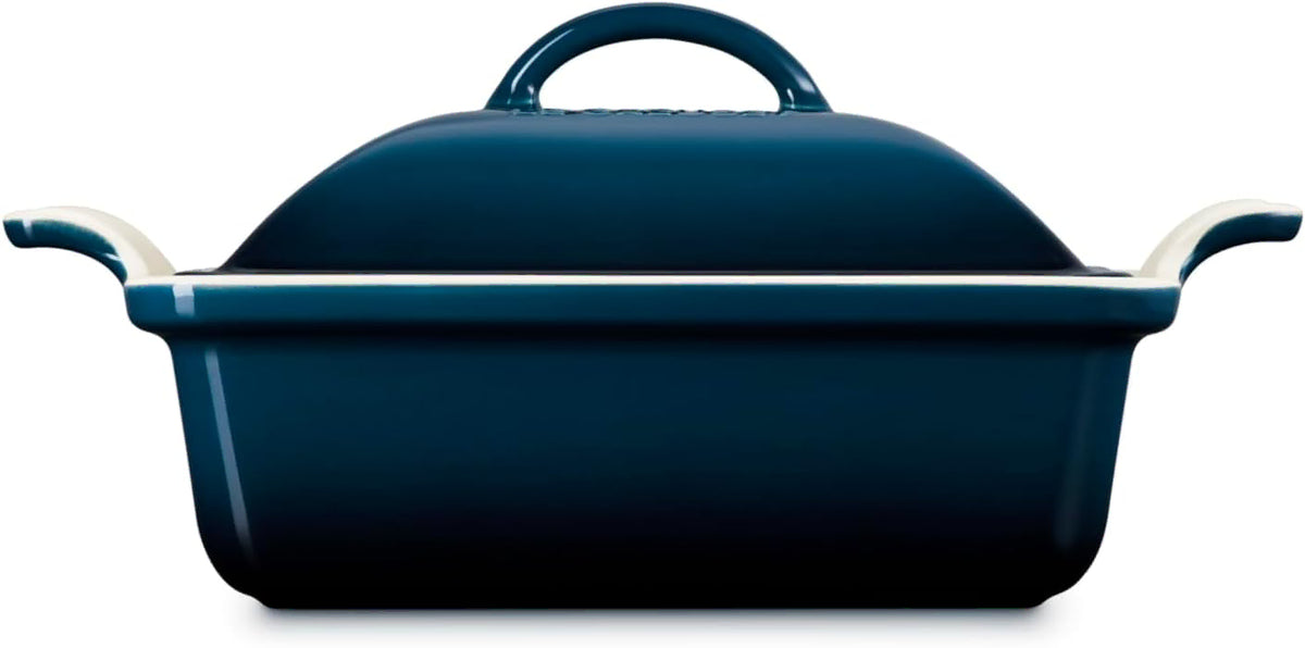 Side view of a dark blue enameled cast iron casserole dish with a lid, featuring cream-colored handles on the sides, shown against a plain white background.