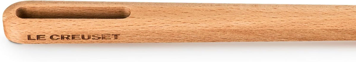 A close-up of a light natural wood paddle or spatula handle with a slot cutout at the top and the brand name 'LE CREUSET' printed in dark lettering on the side.