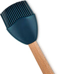 A silicone basting brush with a dark teal-blue head and a light brown wooden handle, shown on a plain white background.