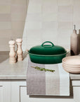 Artichaut casserole dish on a kitchen counter with a towel and herb.