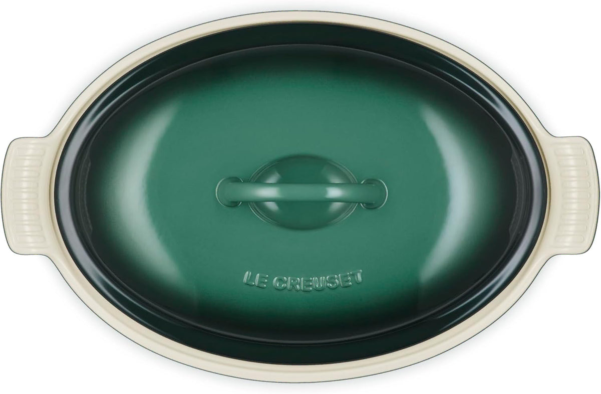 Le Creuset oval lidded casserole dish in dark green with cream-colored handles and rim, shown from a top-down perspective on a white background.