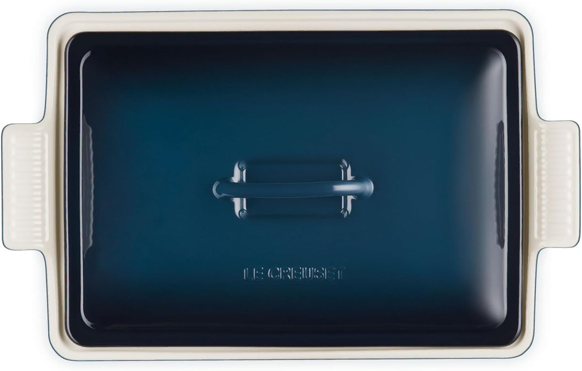 Top view of a rectangular ceramic casserole dish with a matching lid, featuring a deep navy blue interior and a cream-colored exterior with side handles.