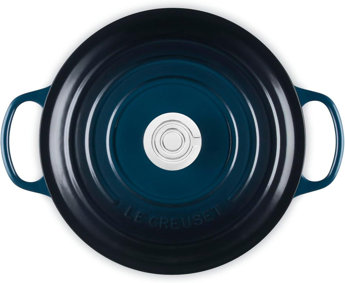 Top-down view of a Le Creuset round enameled cast iron pot with side handles, showing a dark navy blue exterior and a silver metal center knob.