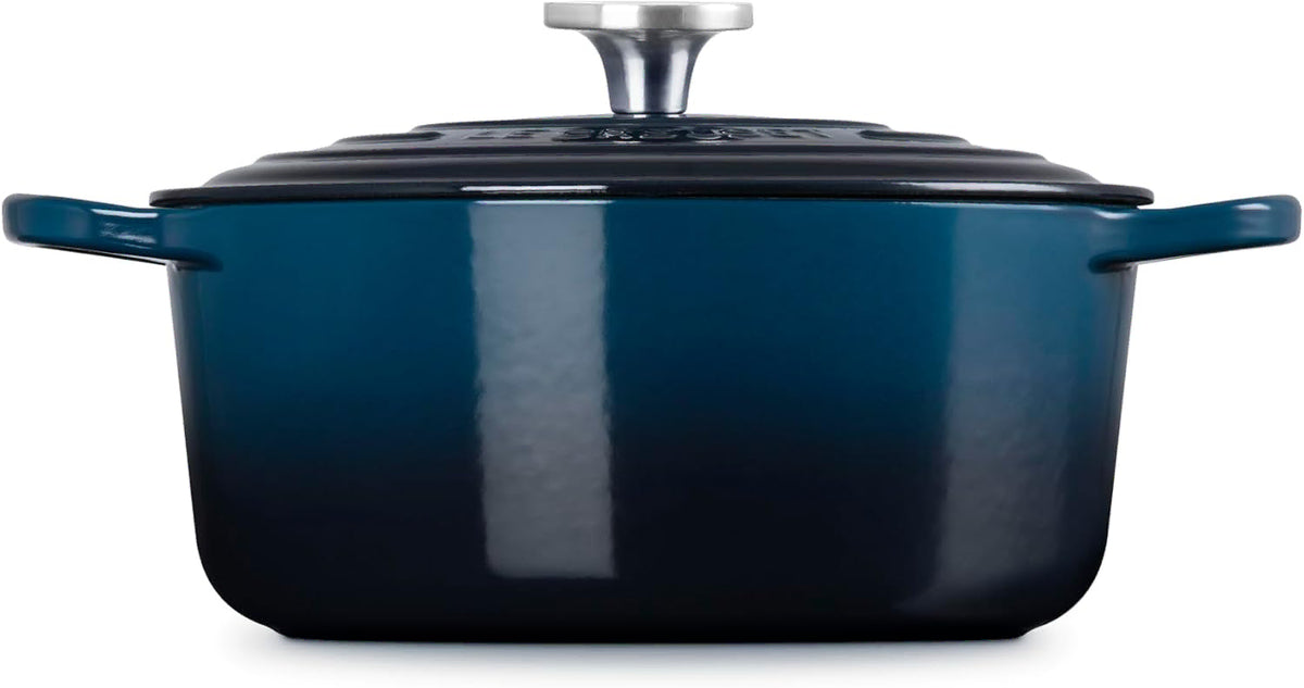 Side view of a dark blue enameled cast iron Dutch oven with a matching lid and silver metal knob, shown on a clean white background.
