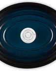 Top view of an oval Le Creuset enameled cast iron Dutch oven with a dark teal blue finish and black rim, featuring side handles and a silver-colored center knob.