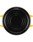 A Le Creuset black cast iron casserole dish with bright yellow handles, shown from a top-down view on a white background.