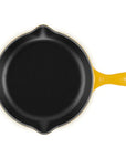 A top-down view of a yellow cast iron skillet with a black non-stick interior, featuring a yellow handle and a small yellow bail on the left side, set against a plain white background.