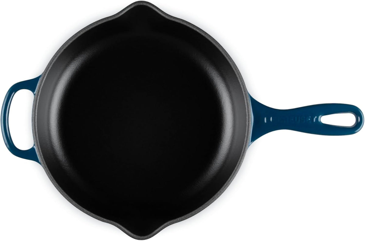 A top-down view of a cast iron skillet with a dark blue enameled handle and side handle, set against a plain white background.