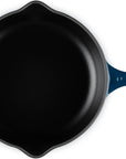 A top-down view of a cast iron skillet with a dark blue enameled handle and side handle, set against a plain white background.