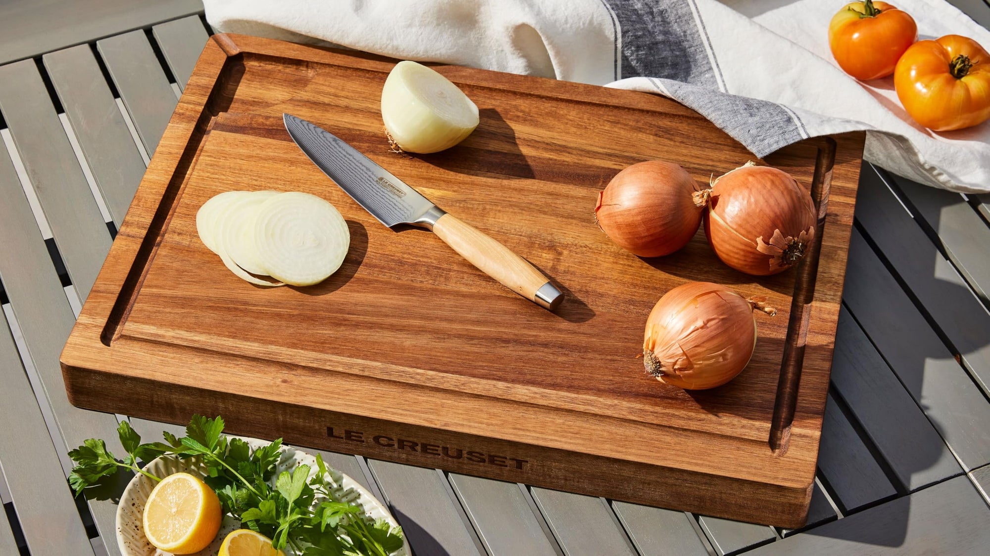 Wooden cutting board with sliced onions, a knife, and tomatoes on a wooden surface.