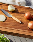 Wooden cutting board with sliced onions, a knife, and tomatoes on a wooden surface.