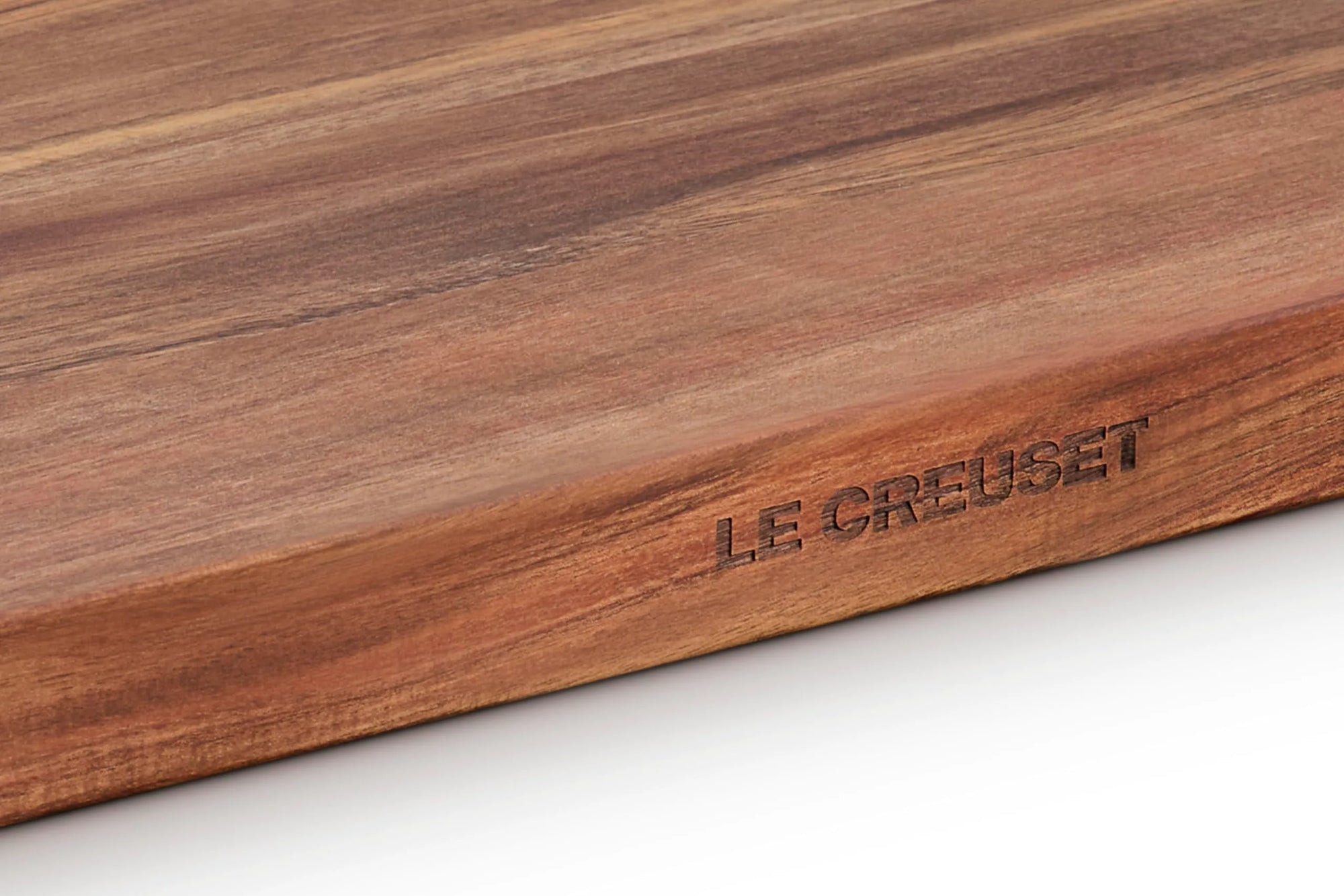 Close-up of a Le Creuset wooden cutting board showing the engraved brand name and rich wood grain texture.